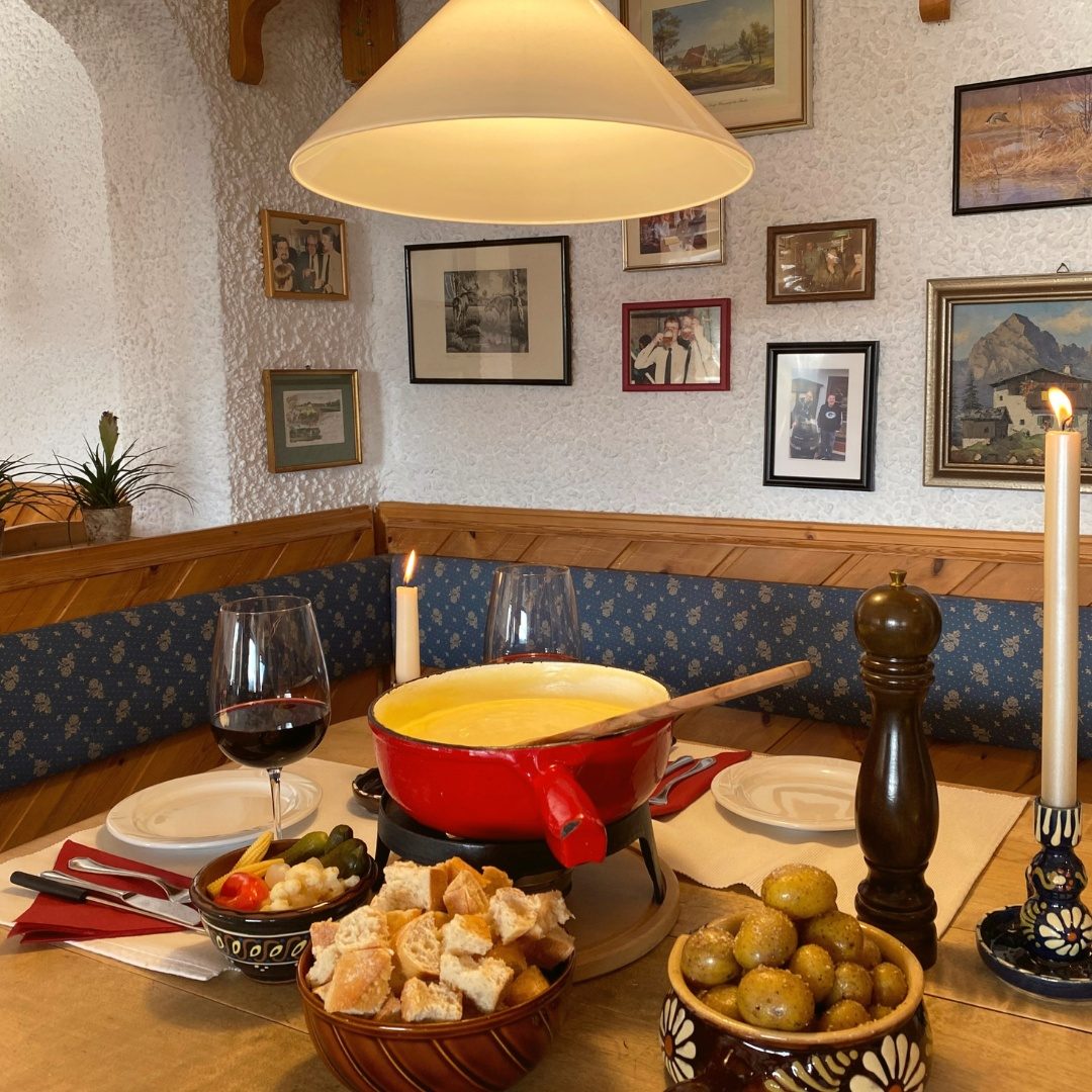 Käsefondue mit Baguette, Wein und Kerzen auf gedecktem Tisch